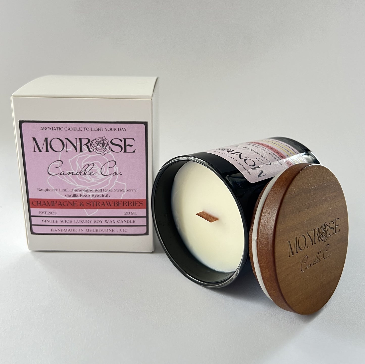 Side view of a black jar candle with "Champagne & Strawberries" fragrance and a cotton wick, containing 185 grams of soy wax and offering 33 hours of burn time.