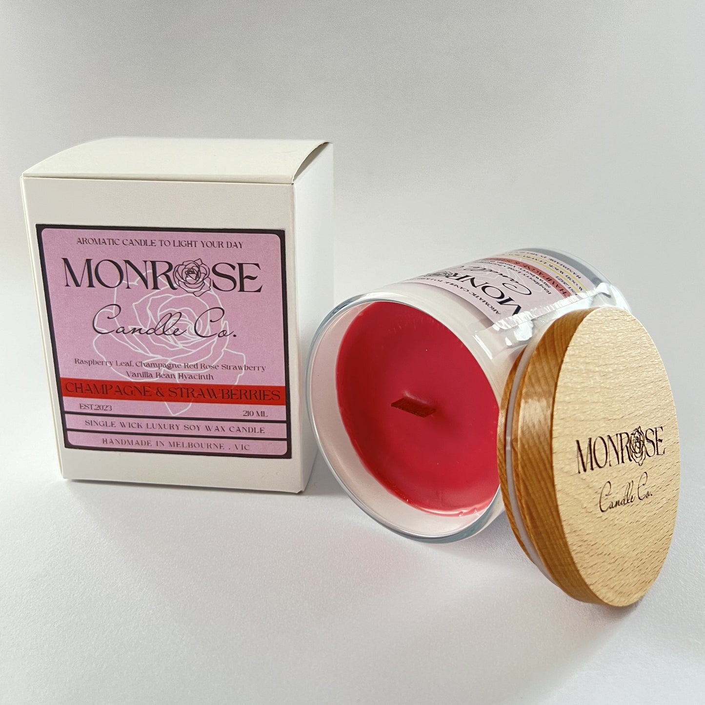 Side view of a white jar candle with Champagne & Strawberries fragrance and a cotton wick, containing 185 grams of soy wax and offering 33 hours of burn time.