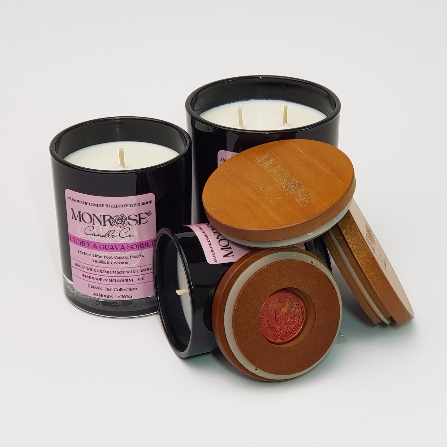 Front view of "Lychee and guava sorbet" fragrance candle collection in black jars with cotton wicks.