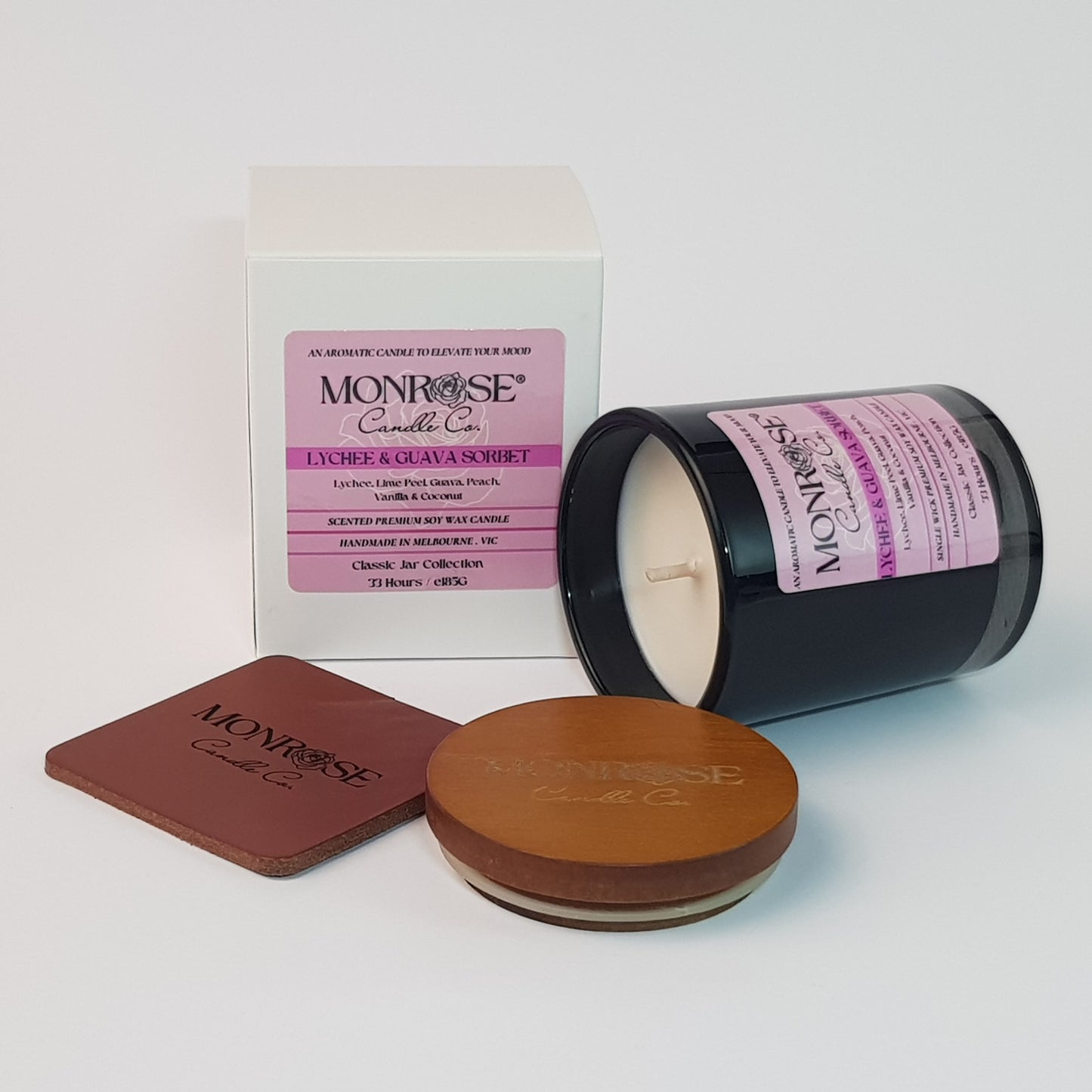 Side view of a container candle with "Lychee & guava sorbet" fragrance in black glass jar and a cotton wick, containing 185 grams of soy wax and offering 33 hours of burn time.