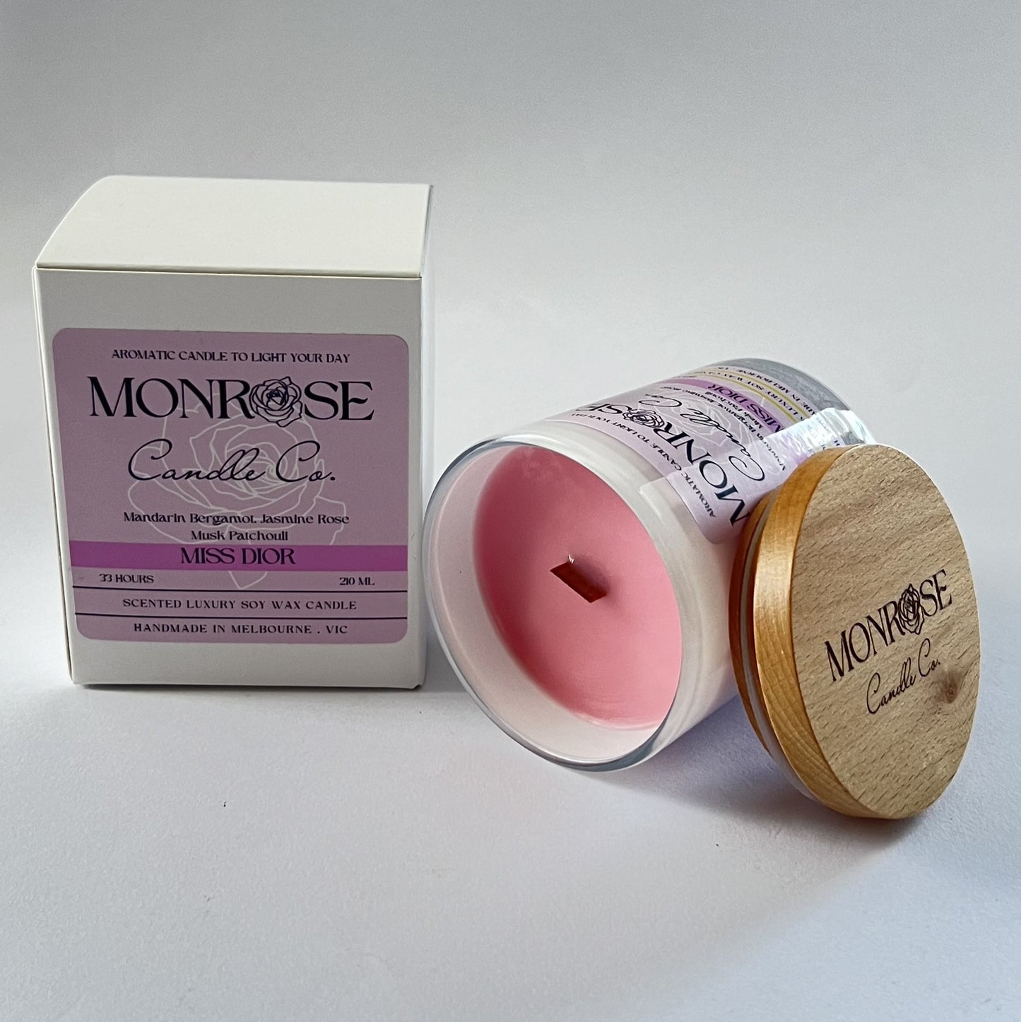 Side view of a white jar candle with "Miss Dior" fragrance and a wood wick, containing 185 grams of soy wax and offering 33 hours of burn time.