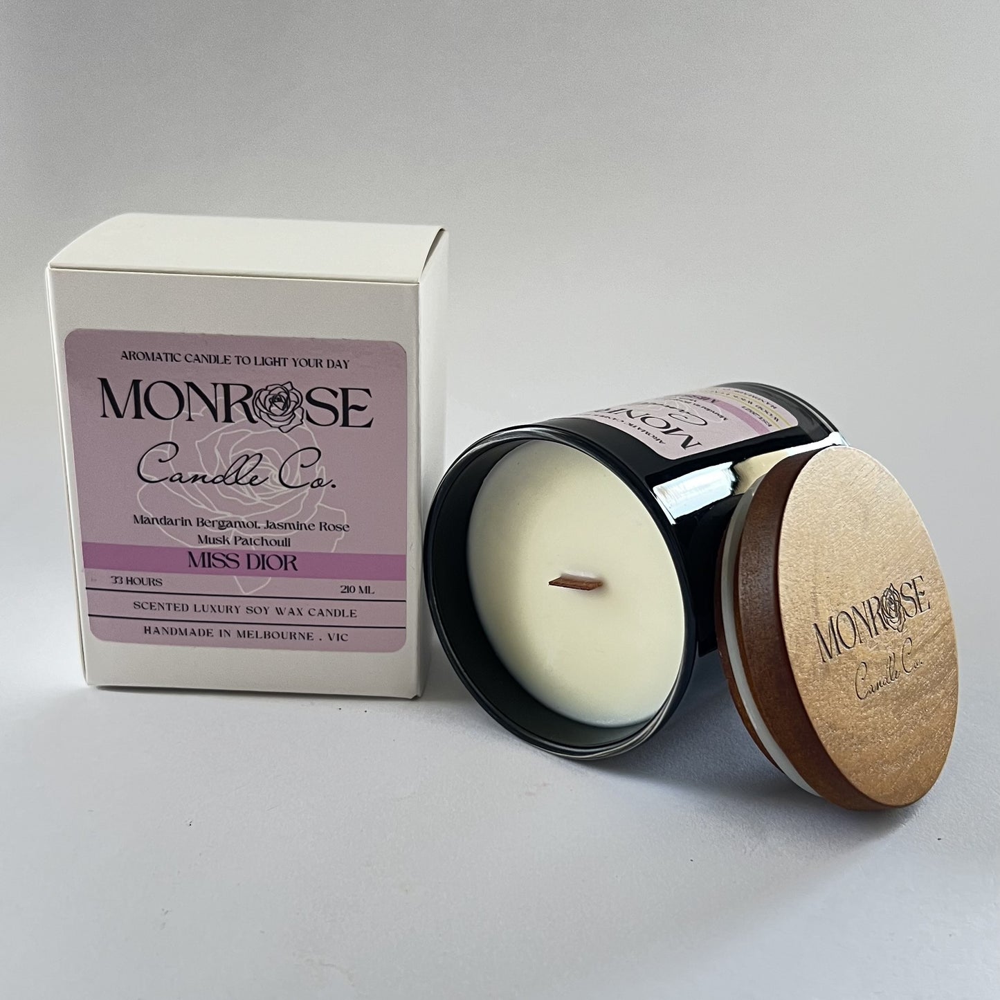 Side view of a black jar candle with "Miss Dior" fragrance and a wood wick, containing 185 grams of soy wax and offering 33 hours of burn time.