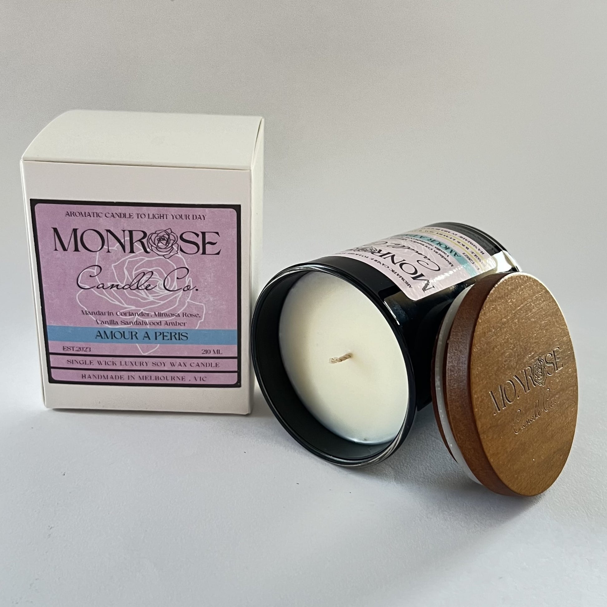 Side view of a black jar candle with "Amour A Paris" fragrance and two cotton wicks, containing 185 grams of soy wax and offering 33 hours of burn time.