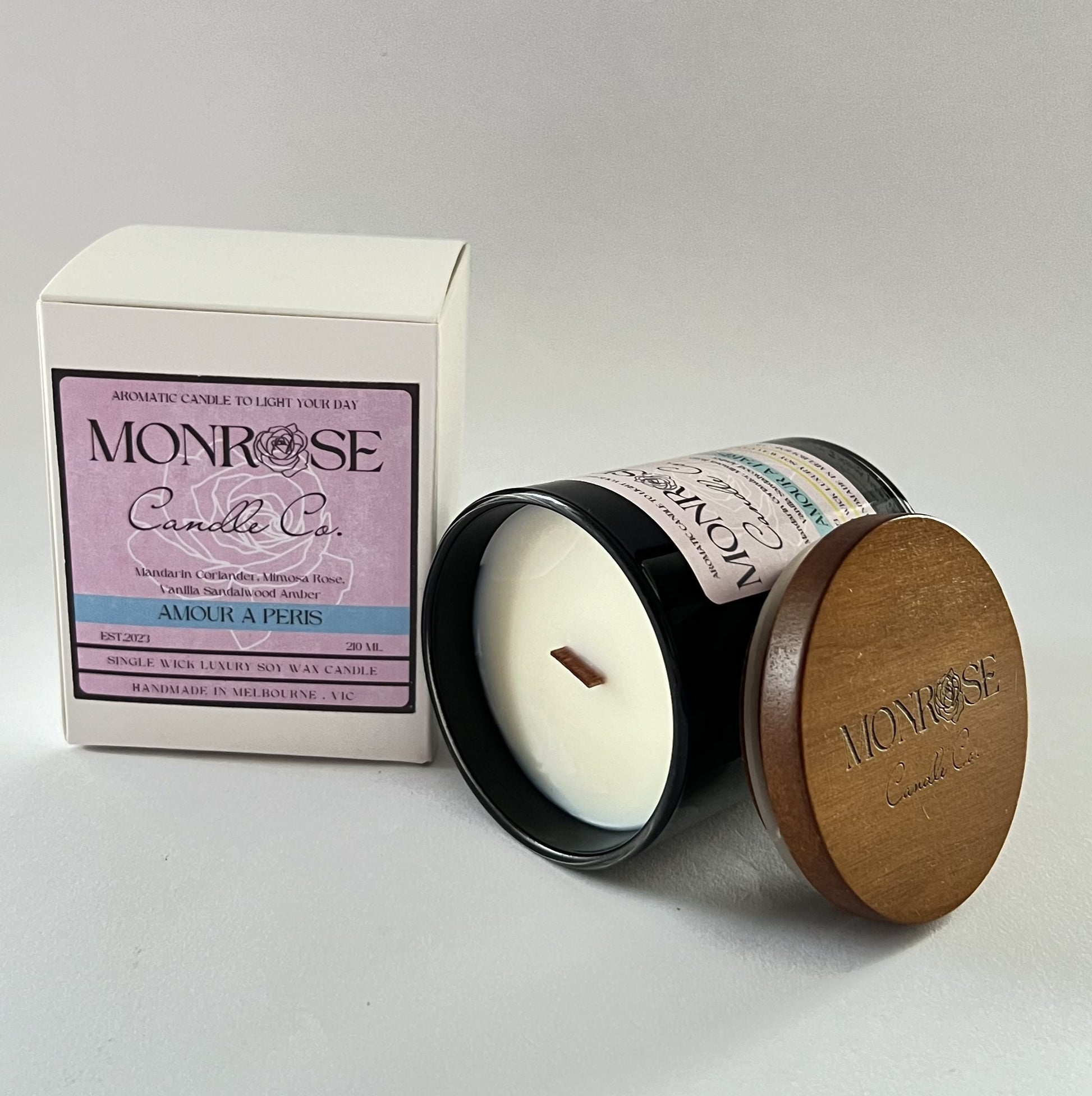 Side view of a black jar candle with "Amour A Paris" fragrance and two wood wicks, containing 185 grams of soy wax and offering 33 hours of burn time.