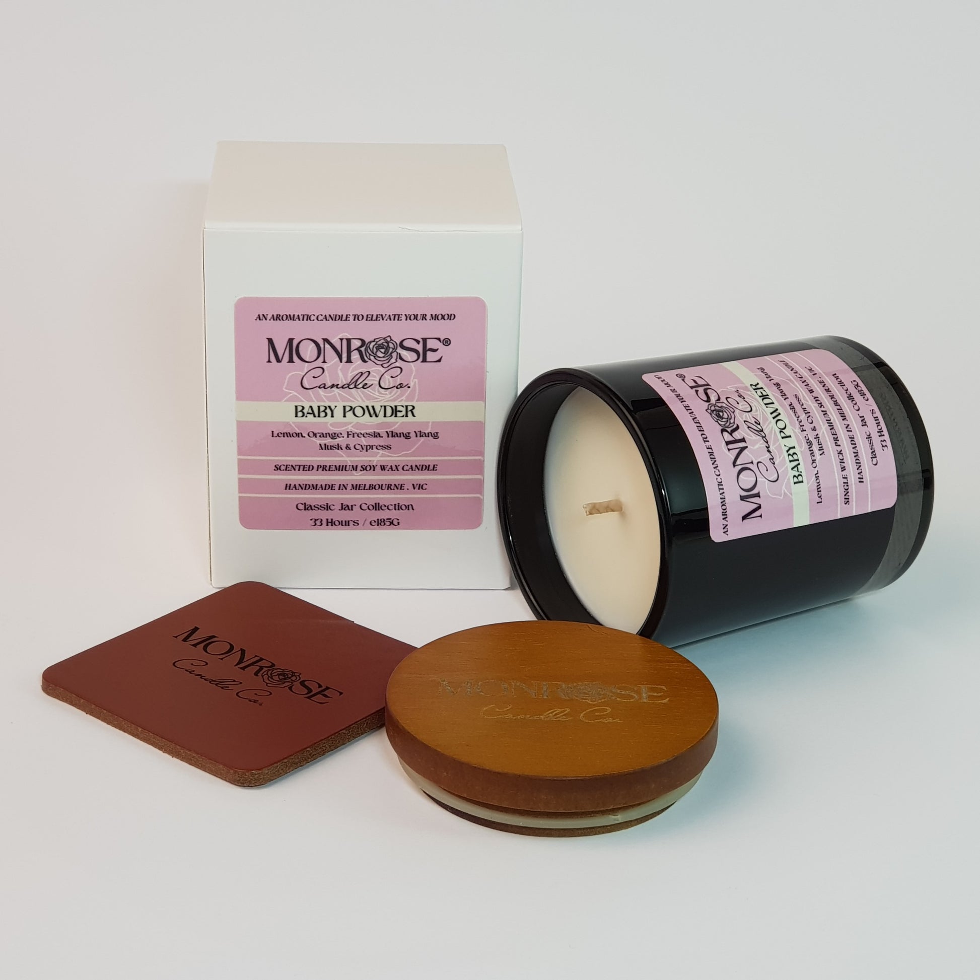 Side view of a black jar candle with "Baby powder" fragrance and a cotton wick, containing 185 grams of soy wax and offering 33 hours of burn time.