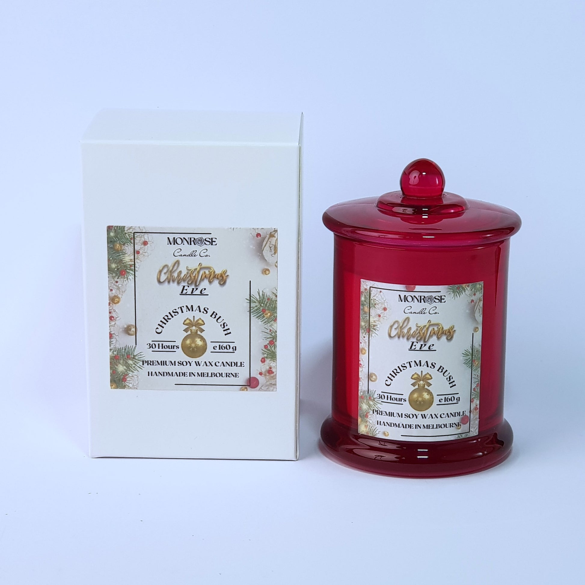 Front view of a red jar candle with 
"Christmas Bush" fragrance and a cotton wick, containing 160 grams of soy wax and offering 30 hours of burn time.