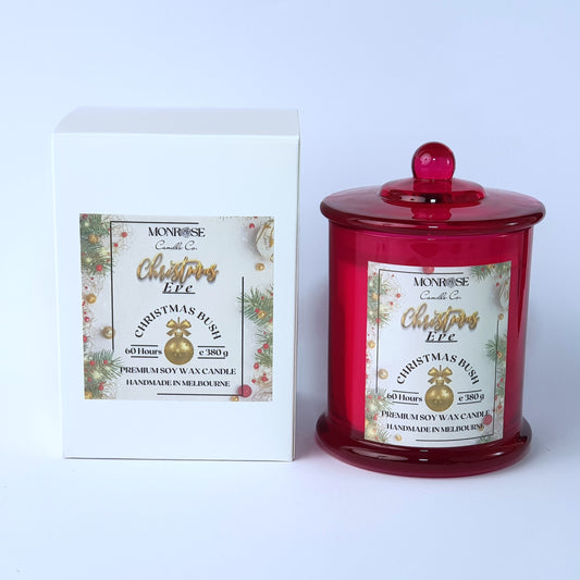 Front view of a red jar candle with 
"Christmas Bush" fragrance and a cotton wick, containing 380 grams of soy wax and offering 60 hours of burn time.