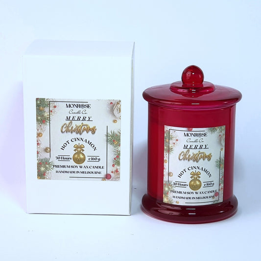This is a front view of a red jar candle with "Hot cinnamon" fragrance and a cotton wick, containing 160 grams of soy wax and offering 30 hours of burn time.