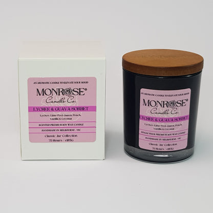 Front view of a container candle with "Lychee & guava sorbet" fragrance in black glass jar and a cotton wick, containing 185 grams of soy wax and offering 33 hours of burn time.
