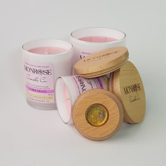 Front view of a candle collection in white jars infused with "Lychee peony" fragrance with cotton wicks.
