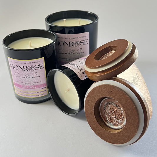 Front view of container candle collection infused with "Miss Dior" fragrance and in black jars with cotton wicks.