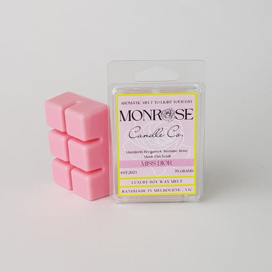 This is the side view of a 6 pack soy wax melt, featuring a pink solid wax melt standing on the left of the packaging. The fragrance of the wax melt is "Miss Dior" and contains 70 grams of soy wax and it is hand crafted in Melbourne, Australia.