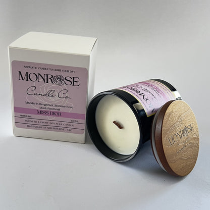 Side view of a black jar candle with "Miss Dior" fragrance and a wood wick, containing 265 grams of soy wax and offering 48 hours of burn time.