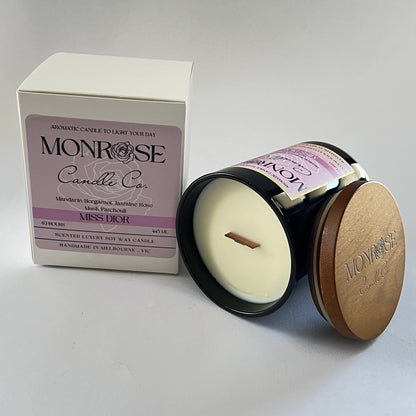 Side view of a black jar candle with "Miss Dior" fragrance and a wood wick, containing 395 grams of soy wax and offering 63 hours of burn time."