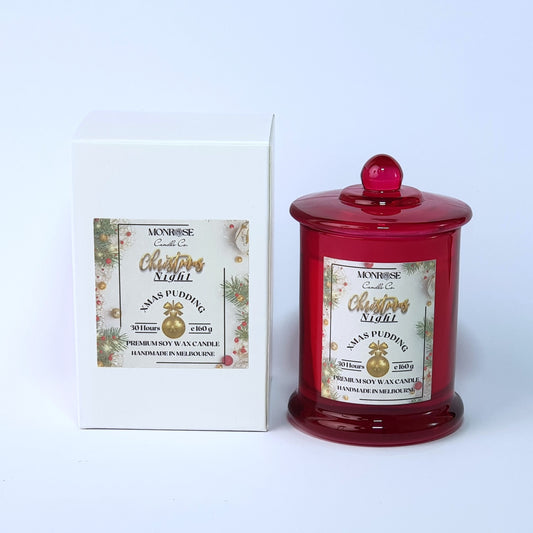 Front view of a red jar candle with 
"Xmas Pudding" fragrance and a cotton wick, containing 160 grams of soy wax and offering 30 hours of burn time.